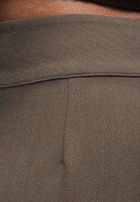 Gros plan sur une couture en tissu marron d'un vêtement, montrant une texture détaillée en sergé diagonal.