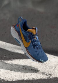 Blå løbesko med mesh overdækkende, gul swoosh-logo og brun sål. Har teksturerede detaljer, blå snørebånd og plettet mellemsål.