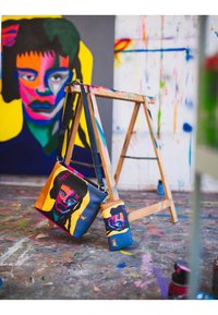 Bunte Kunsttaschen mit abstrakten Gesichtsmotiven, darunter eine große Schultertasche und ein kleinerer Geldbeutel, beide aus glattem, strapazierfähigem Material gefertigt.