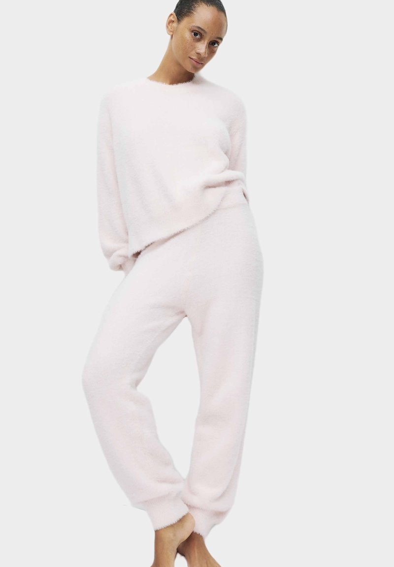 Jasnoróżowy, puszysty zestaw swetra i spodni; luźny krój, długie rękawy, elastyczne mankiety, miękka tekstura, casualowy design.