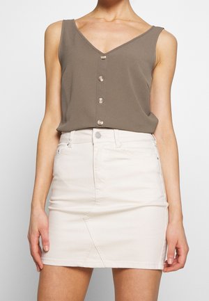 Bez rękawów top w kolorze taupe z guzikami i dekoltem w serek, zestawiony z białą mini spódnicą z wysokim stanem z denimu na stojącej osobie.