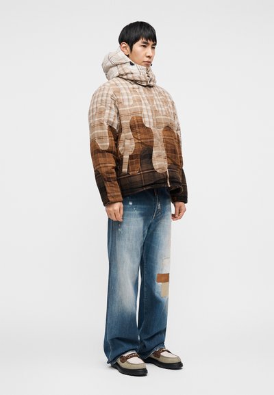 Επενδυμένο καρό μπουφάν σε μπεζ και καφέ αποχρώσεις, με ψηλό γιακά και κουκούλα. Συνδυάζεται με φθαρμένο μπλε τζιν και παπούτσια με μπεζ λεπτομέρειες.