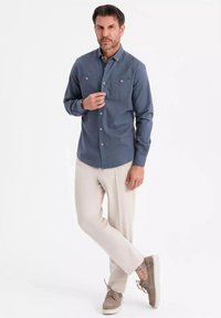 Button-up Hemd aus dunkelblauem Baumwollstoff mit zwei Brusttaschen, kombiniert mit hellbeigen Hosen und braunen Wildlederschuhen.