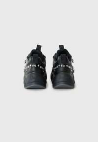 Sorte sneakers med en glat, struktureret overdel, der har skinnende nitter og en kraftig sål. Logo prægede på siden.