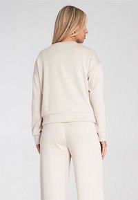 Jasnobeżowa bluza z luźnym krojem, okrągłym dekoltem, długimi rękawami i ściśniętym dołem. Materiał wydaje się być miękki i gładki w dotyku.