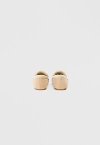 Μπεζ σουέτ παντόφλες με μαλακό, επενδεδυμένο με γούνα εσωτερικό και στρογγυλή πλάτη. Οι επίπεδες σόλες προσφέρουν άνετη εφαρμογή για χρήση σε εσωτερικούς χώρους.