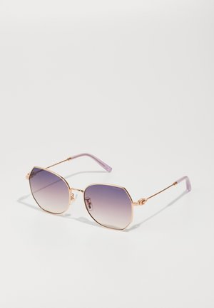 Óculos de sol de metal dourado com uma armação hexagonal e lentes graduadas em roxo. Apresenta hastes finas com uma ponta em roxo claro.