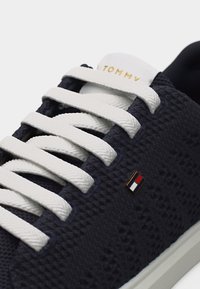 Πλεκτό αθλητικό παπούτσι σε ναυτικό μπλε με λευκά υφασμάτινα κορδόνια, λευκή σόλα, χρυσή επιγραφή "TOMMY" στη γλώσσα και μικρό κόκκινο, λευκό και μπλε λογότυπο Tommy Hilfiger στο πλάι.