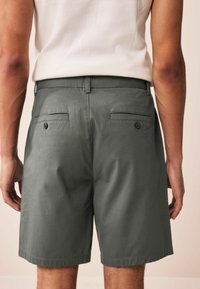 Grau Shorts aus weichem Stoff, ausgestattet mit zwei hinteren Taschen mit Knöpfen, Gürtelschlaufen und einem geraden Saum am unteren Ende.