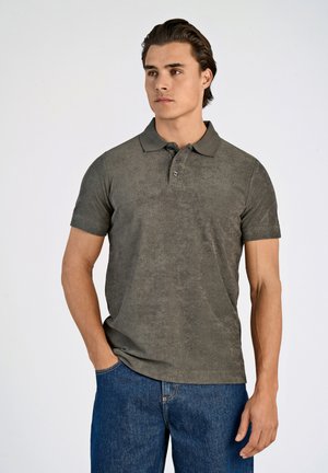 Polo de un verde oliva hecho de tela texturizada, con un cuello clásico, mangas cortas y una tapeta de tres botones, combinado con unos jeans azules.