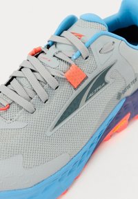 Grau laufschuh aus atmungsaktivem Mesh mit einer blauen und orangen Sohle. Merkmale sind ein strukturiertes Design und reflektierende Akzente.