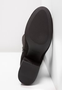 Černé semišové kotníkové boty s texturovanou gumovou podrážkou, s bočním zipem a kulatou špičkou. Logo viditelné na podrážce.