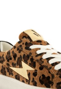 Zapatilla deportiva de estampado de leopardo marrón con textura peluda, cordones blancos, acento de rayo dorado y suela de goma blanca. Vista en primer plano.