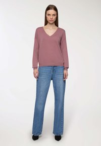 Pullover rosa a V con maniche lunghe, abbinato a jeans a gamba dritta a vita alta di colore blu chiaro. Scarpe nere completano l'outfit.