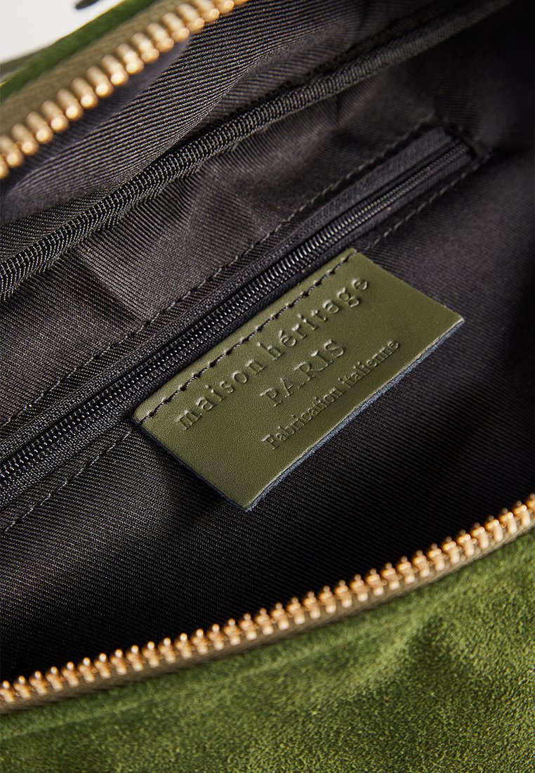 Grüner Wildlederbeutel mit schwarzem Innenraum, ausgestattet mit einem goldenen Reißverschluss und einem Etikett, das "maison héritage PARIS" geprägt hat.