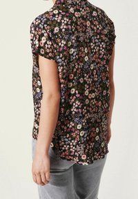 Korte mouw blouse van zwarte stof versierd met kleurrijke bloemmotieven, met een kraag en een gebogen zoom.