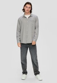 Grijze button-up shirt met een borstzak, gecombineerd met donkergrijze jeans en witte sneakers. De stof lijkt soepel en licht van gewicht.