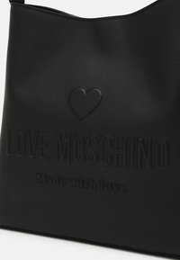 Črna torbica iz umetnega usnja z vrezanim besedilom "LOVE MOSCHINO" in poudarkom v obliki srca, z gladko teksturo in odprtim vrhnjim dizajnom.