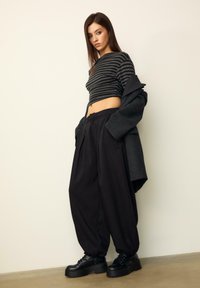 Čierne oversized nohavice a skrátený čierno-sivý pruhovaný top, v kombinácii s masívnymi čiernymi topánkami. Tmavý kabát je prehodený cez plecia.