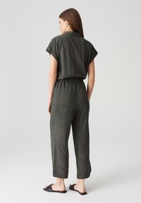 Schwarzer Jumpsuit mit kurzen Ärmeln, elastischem Bund und cropped Beinen. Hat ein dezentes Muster und eine lockere Passform. Kombiniert mit schwarzen Sandalen.