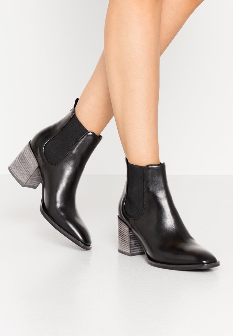 Stivaletti neri in pelle con pannelli laterali elasticizzati, caratterizzati da un tacco a blocco grigio testurizzato e una punta appuntita.