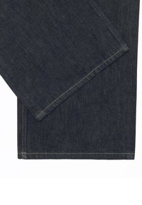 Tissu en denim bleu foncé plié avec des coutures visibles le long des bords sur un fond blanc.