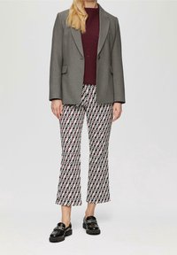 Grijze blazer met notch-lapels, bordeaux ribgebreide trui, gestreepte witte en maronenkleurige flared broeken, en zwarte loafers met hardware-accenten.
