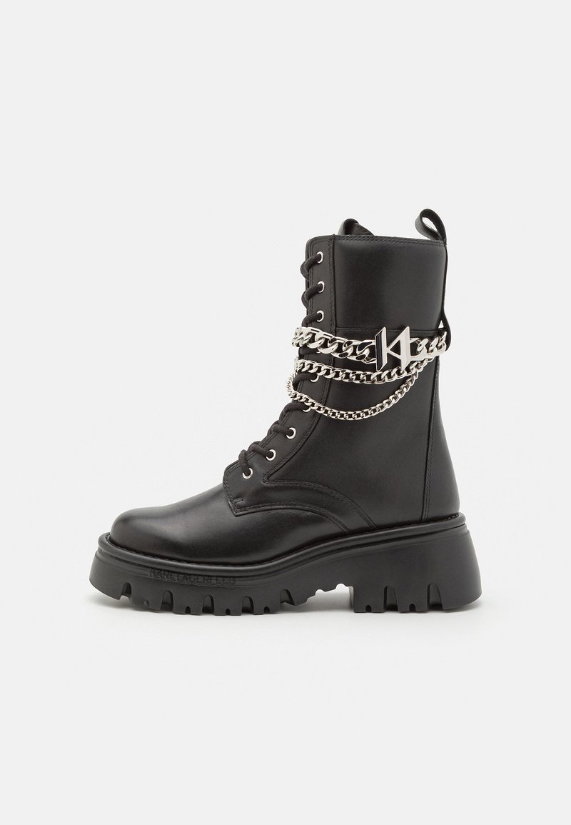 Schwarze Leder-Ankle-Boots mit einer groben Sohle, versehen mit silbernen Kettenakzenten und Logo-Detail, Schnürdesign und einer Zuglasche an der Rückseite.