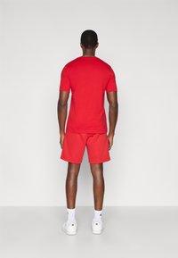 Κόκκινο βαμβακερό t-shirt με κοντά μανίκια, συνοδευόμενο από αντίστοιχο κόκκινο σορτς. Απλός, χωρίς διακοσμήσεις σχεδιασμός, απεικονιζόμενο από πίσω σε ουδέτερο φόντο.