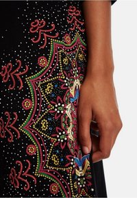 Svart plagg med färgglad blommig broderi i röda, gröna, blå och gula nyanser, med prickiga accenter och intrikata detaljer.