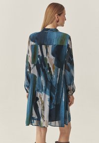 Langärmliges, plissiertes Kleid mit einem Aquarellmuster in Blau, Grün und Weiß. Hergestellt aus leichtem Stoff mit einem Kragen und Knopfdetails.