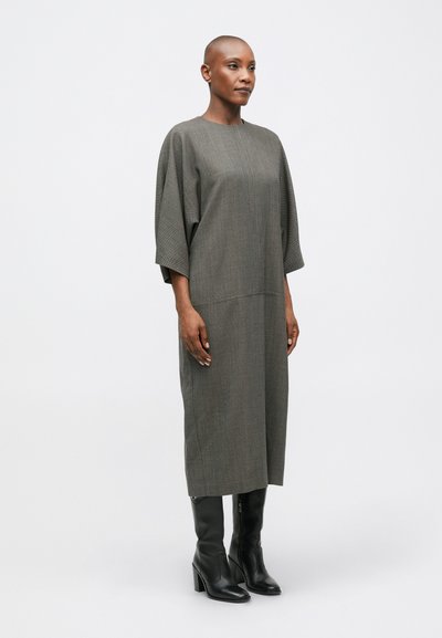 Szürke, térd hosszúságú ruha laza szabással, ejtett vállakkal és függőleges textúrával; magas sarkú fekete csizmával párosítva.