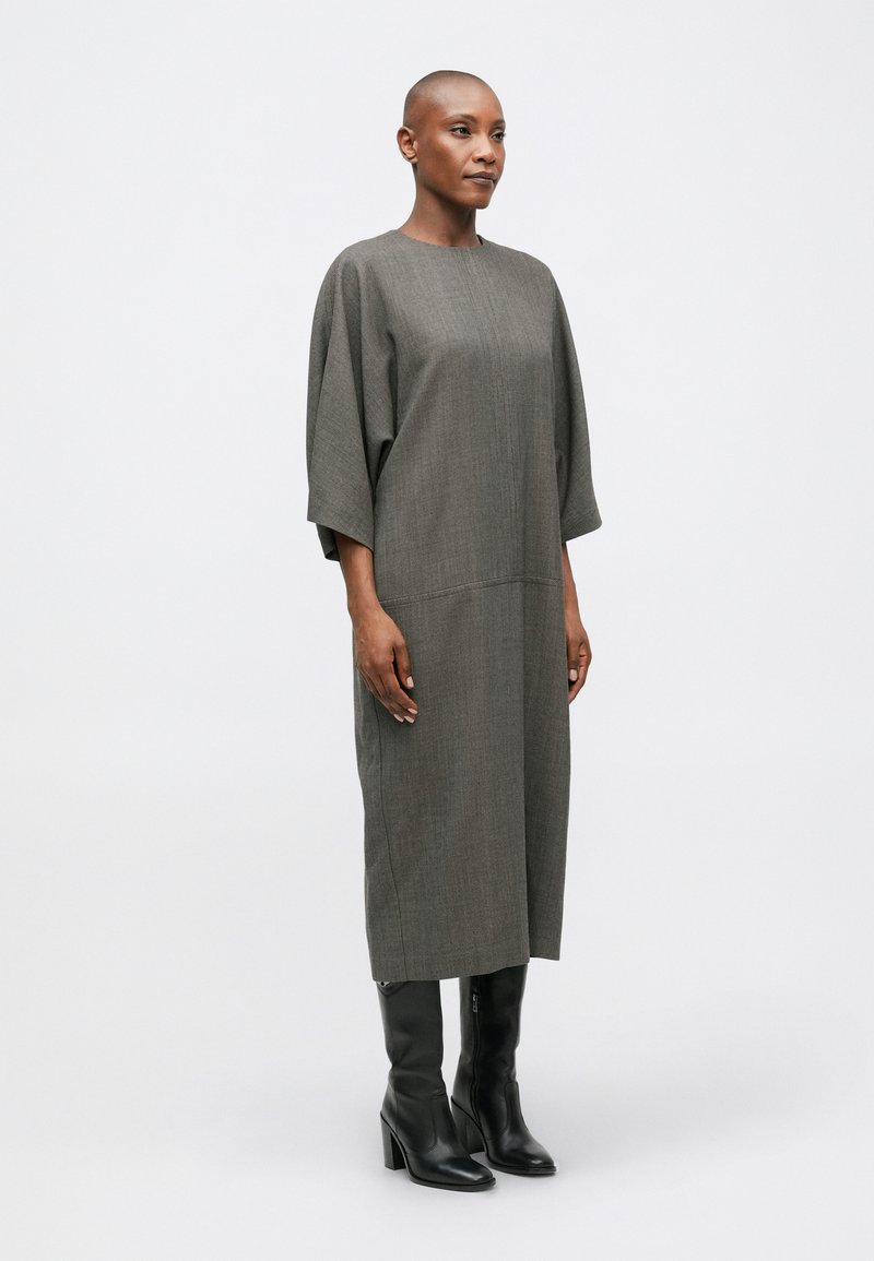 Robe grise, longueur genou, avec une coupe ample, des épaules dénudées et une texture verticale ; assortie à des bottes noires à talons hauts.
