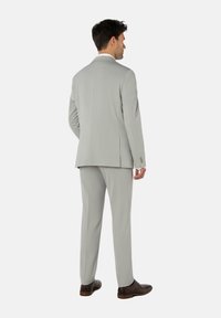 Costume gris avec une coupe ajustée, tissu texturé, revers crantés et fente unique ; associé à des chaussures brunes.