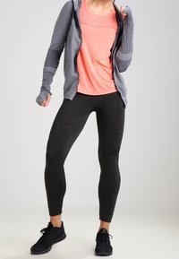 Tenue de sport comprenant un sweat à capuche zippé gris, un haut à manches courtes rose et un legging moulant noir, associé à des chaussures de sport noires.