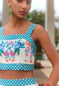 Krém színű, virágmintás crop top türkiz geometrikus részletekkel és pántokkal. Hímzett virágok találhatók rajta rózsaszín, kék és zöld színekben.