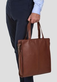 Borsa a tote in pelle marrone con finitura testurizzata, dotata di due manici corti, chiusura con cerniera e dettagli di cucitura verticale.