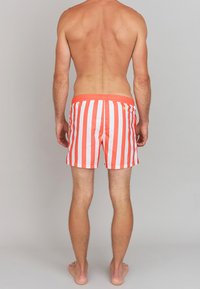 Shorts de bain à rayures verticales rouges et blanches avec une taille élastique, des coutures visibles et un petit logo jaune à l'arrière.