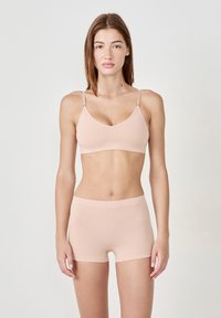 Sostén sin costuras de un suave color rosa claro con tirantes ajustables y pantalones cortos de cintura alta a juego. Tejido suave y elástico con una textura lisa.
