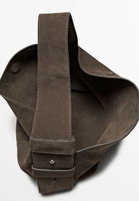 Brown suede handbag with a wide shoulder strap, featuring a stitched edge and a button closure. The interior is soft-textured and spacious.
