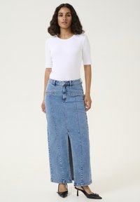 Denim maxi skirt in light blue, featuring front slit, two pockets, and a high waistband. Paired with a fitted white top and black heels.