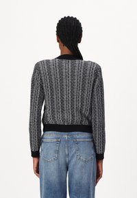 Svart och vit stickad tröja med ribbad textur, långa ärmar och svart midja. Bärs tillsammans med ljusblå, något lös passande jeans.