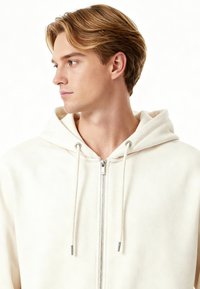 Felpa con cappuccio chiara con cerniera, dalla texture morbida, caratterizzata da cappuccio con coulisse e dettagli in metallo sulla cerniera. Design semplice e minimalista.