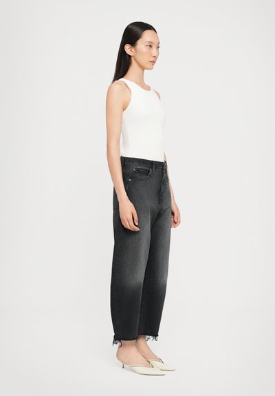 White ribbed sleeveless top paired with high-waisted black denim jeans, featuring frayed hems. Model wearing light-colored slip-on shoes.