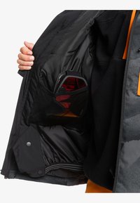 Intérieur d'une veste noire isolée avec un accent orange et une poche en mesh contenant des lunettes teintées de rouge. Texture lisse et forme ajustée.
