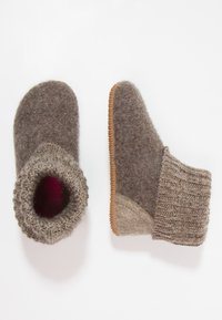Wollen slippers in grijstinten met een gebreide rand, ronde vorm en een textureer zool. Zacht interieur met een maroon accent zichtbaar.