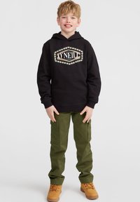 Svart hoodie med vit och guld grafisk logotyp, gröna cargo byxor med sidofickor och beige stövlar. Enkelt design, avslappnad passform.