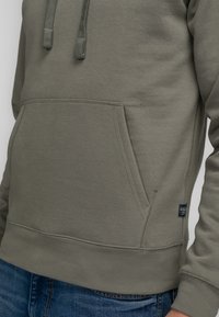 Sudadera de color verde olivo hecha de una suave mezcla de algodón, con un bolsillo tipo canguro en la parte delantera, capucha con cordón, y mangas y bajo acanalados.