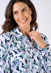 Langarmshirt met een button-down kraag, voorzien van een veelkleurig bladerenpatroon in tinten van blauw, paars en wit tegen een lichte achtergrond.