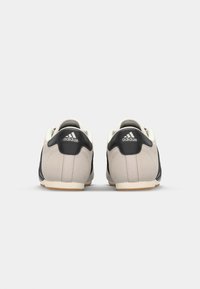 Adidas čevlji z zgornjim delom iz svetlo sive nubuk usnje, črnimi usnjenimi dodatki, belim ovratnikom in gumijastim podplatom. Logotip prikazan na peti.